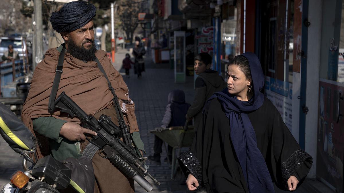 A Taliban fighter stands guard as a woman walks past in Kabul. | Photo Credit: AP | The Hindu